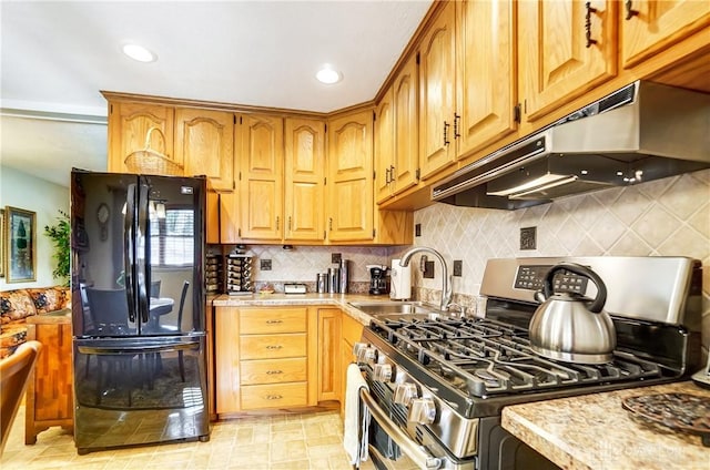 kitchen with light countertops, freestanding refrigerator, a sink, stainless steel gas range, and under cabinet range hood