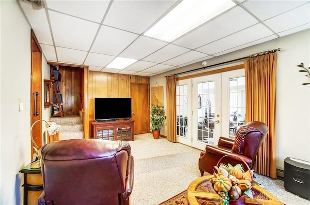 living room featuring carpet, french doors, a drop ceiling, and wood walls