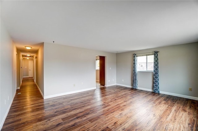 spare room featuring baseboards and dark wood-style flooring