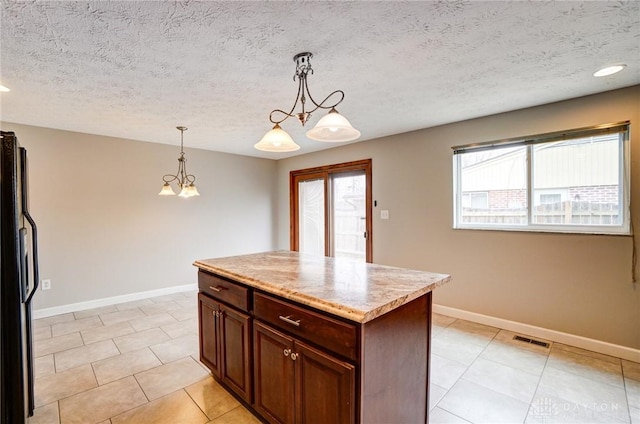 kitchen with a kitchen island, visible vents, baseboards, hanging light fixtures, and freestanding refrigerator