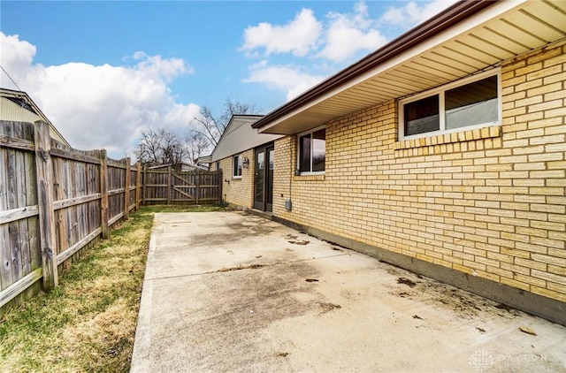 view of side of property featuring a patio, brick siding, and fence