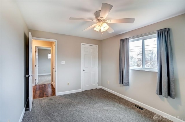 unfurnished bedroom featuring dark colored carpet, visible vents, ceiling fan, and baseboards