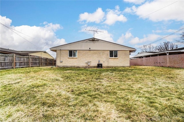 back of property featuring a fenced backyard, a lawn, and brick siding