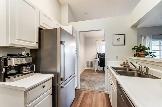 kitchen with white cabinets, wood finished floors, stainless steel appliances, light countertops, and a sink