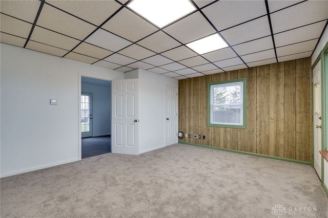 carpeted spare room featuring wood walls, a drop ceiling, and a wealth of natural light