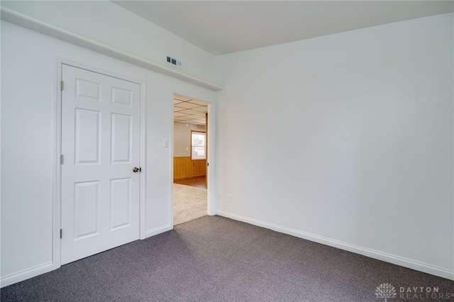 unfurnished room with a paneled ceiling, visible vents, dark carpet, wainscoting, and wooden walls