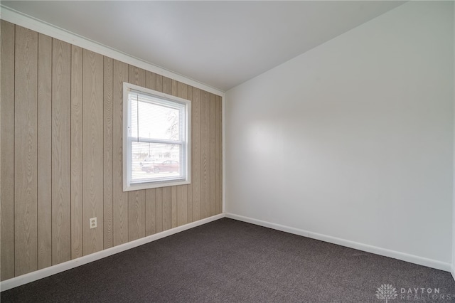 unfurnished room with wooden walls, dark carpet, and baseboards