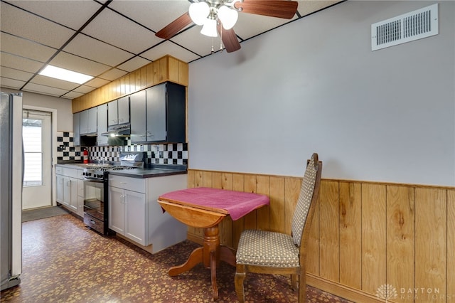 kitchen with a paneled ceiling, under cabinet range hood, a wainscoted wall, visible vents, and black range with gas stovetop