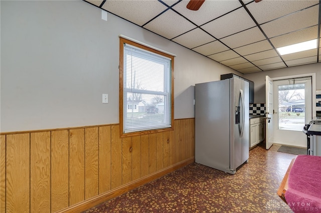 kitchen featuring wooden walls, a drop ceiling, wainscoting, tile patterned floors, and stainless steel appliances