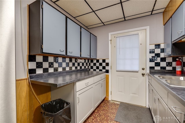 kitchen with decorative backsplash, a drop ceiling, dark countertops, dark floors, and a sink