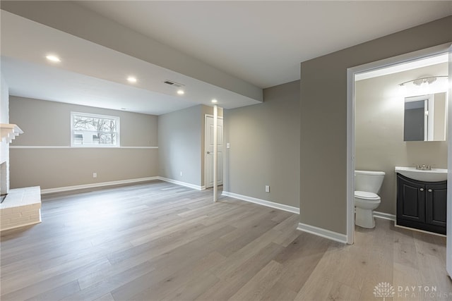 basement with light wood finished floors, a sink, visible vents, and baseboards