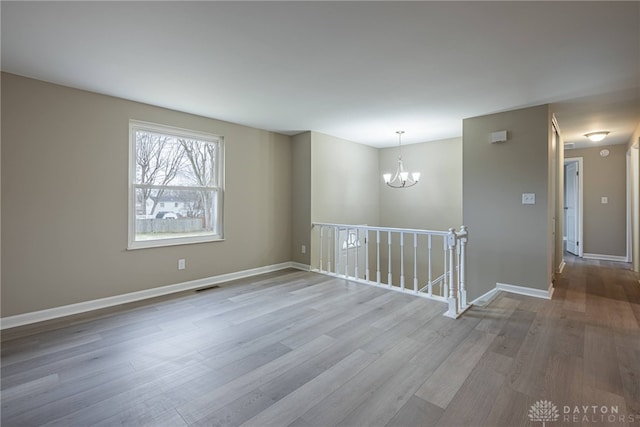 unfurnished room featuring baseboards, visible vents, an inviting chandelier, and wood finished floors