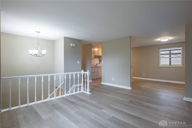 unfurnished room with an inviting chandelier, a sink, baseboards, and wood finished floors