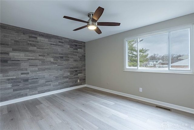 spare room featuring an accent wall, wood finished floors, a ceiling fan, visible vents, and baseboards