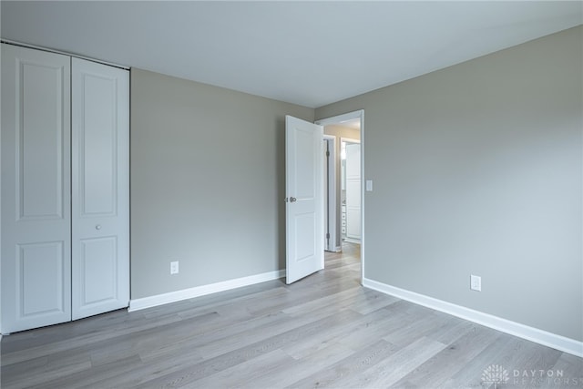 unfurnished bedroom featuring light wood-style floors, baseboards, and a closet