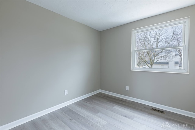 empty room featuring light wood-type flooring, baseboards, and visible vents