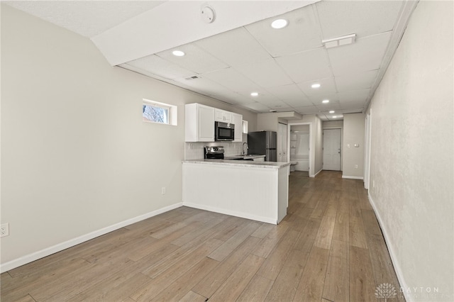 kitchen featuring appliances with stainless steel finishes, light wood-style floors, white cabinetry, a peninsula, and baseboards