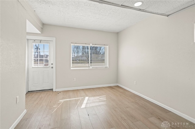 interior space featuring light wood-type flooring, a healthy amount of sunlight, a textured ceiling, and baseboards