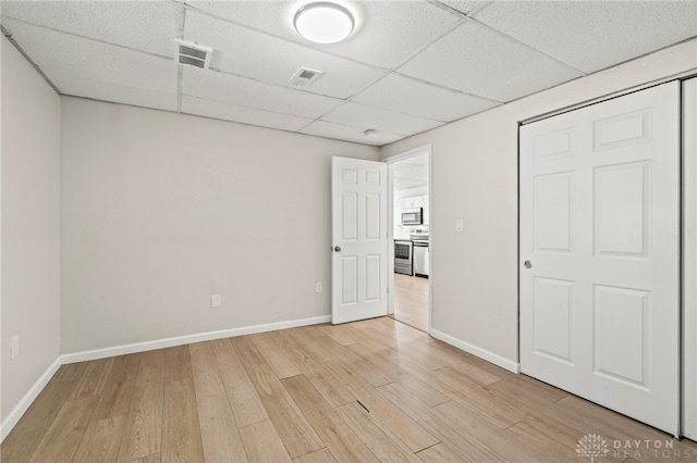 unfurnished bedroom featuring visible vents, light wood-style flooring, baseboards, and a drop ceiling