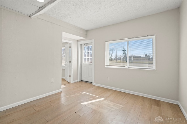 unfurnished room featuring light wood-style flooring, baseboards, and a textured ceiling