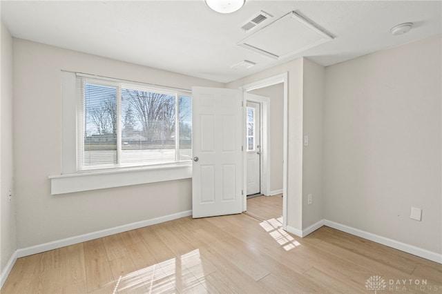 spare room with light wood-style floors, attic access, visible vents, and baseboards