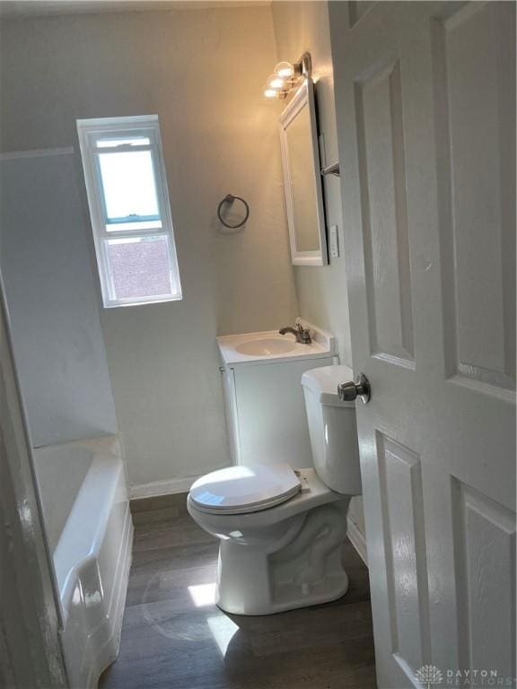 bathroom with toilet, wood finished floors, vanity, baseboards, and a bathtub