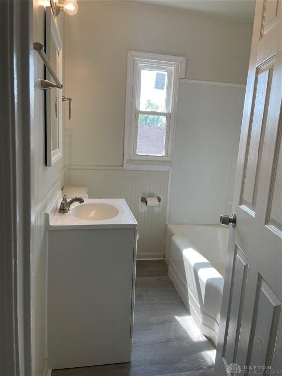 full bathroom featuring vanity, a washtub, wood finished floors, and wainscoting