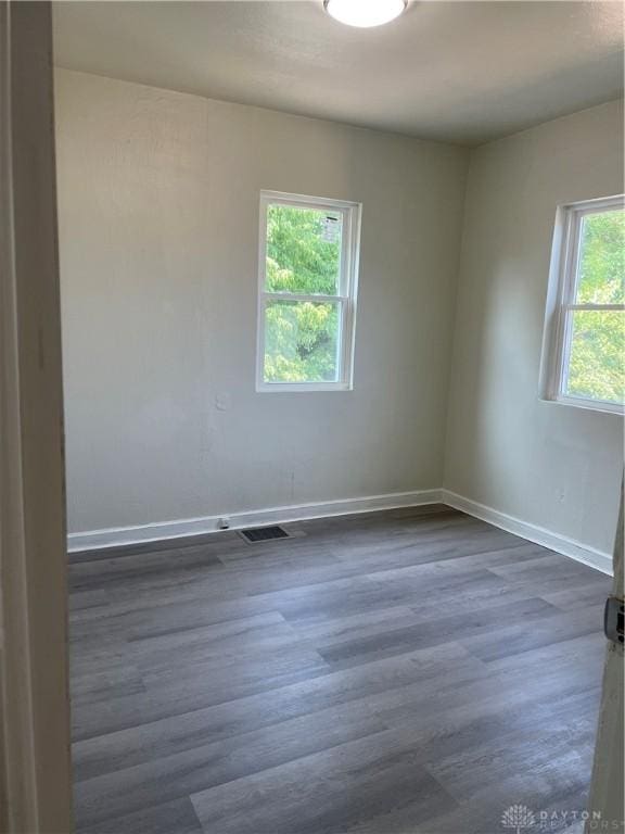 spare room with dark wood-style floors, visible vents, and baseboards