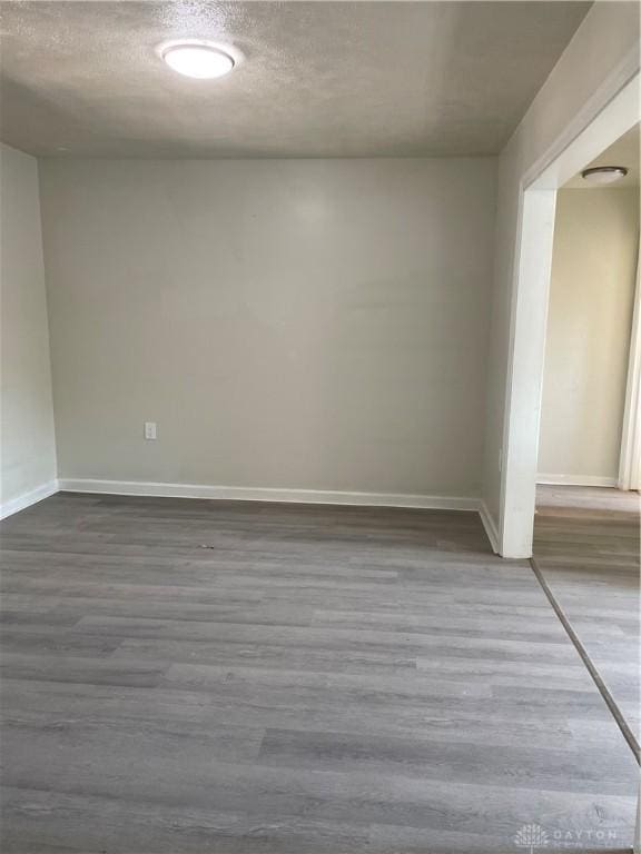 empty room with a textured ceiling, dark wood-style flooring, and baseboards