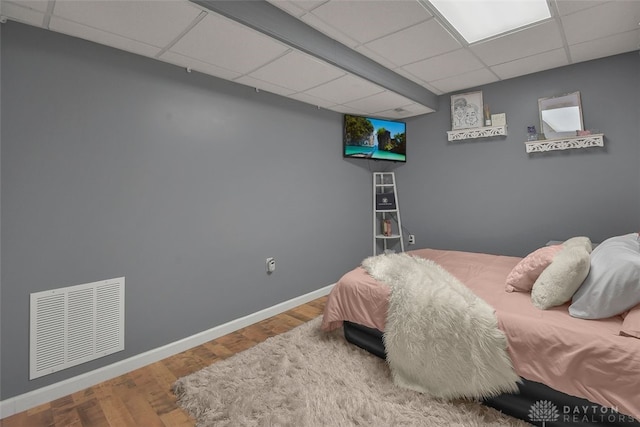 bedroom with baseboards, visible vents, a drop ceiling, and wood finished floors