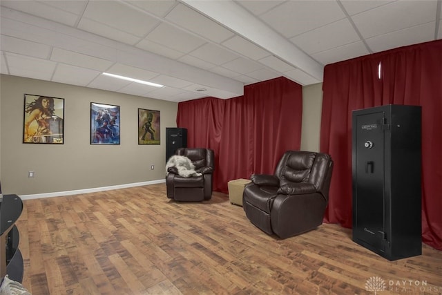 living area with a drop ceiling, wood finished floors, and baseboards