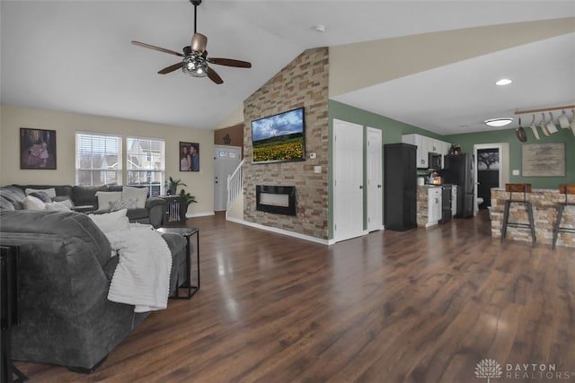 living area featuring a large fireplace, ceiling fan, vaulted ceiling, and dark wood-type flooring