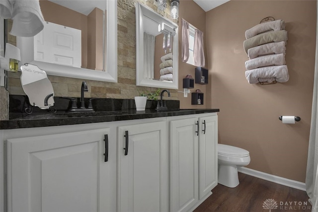 bathroom with toilet, a sink, baseboards, backsplash, and double vanity