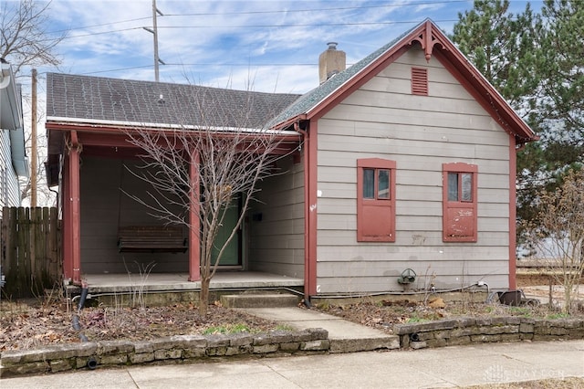 view of home's exterior featuring a shingled roof, a chimney, a porch, and fence