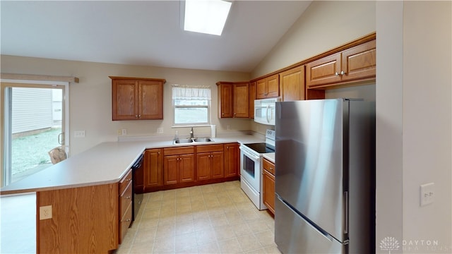 kitchen with white appliances, vaulted ceiling with skylight, brown cabinets, a peninsula, and a sink