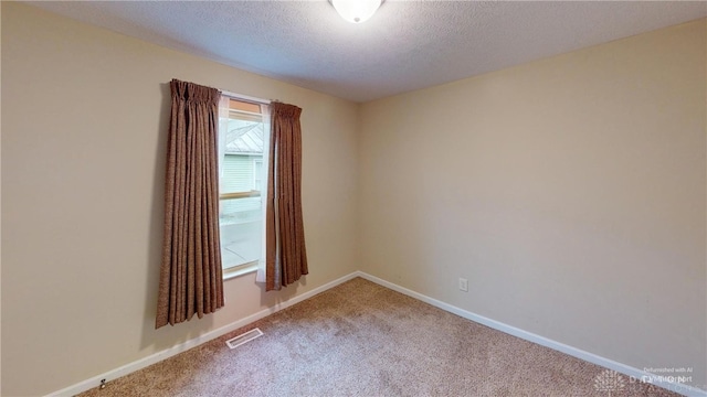 spare room featuring baseboards, carpet, visible vents, and a textured ceiling