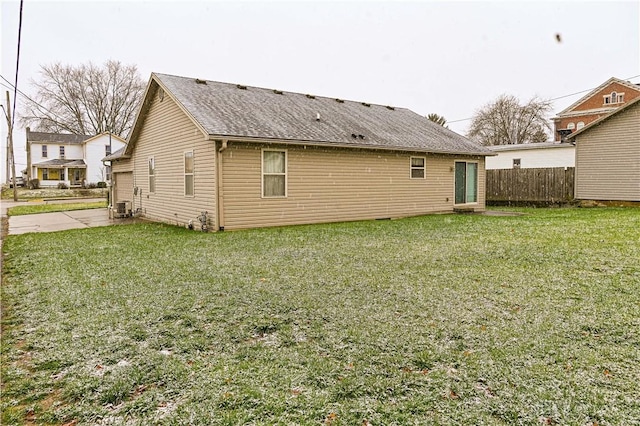 rear view of house with cooling unit, roof with shingles, a yard, and fence