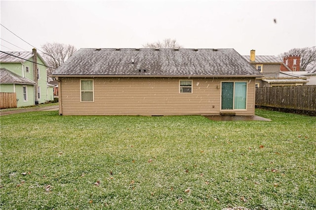 back of property with a shingled roof, fence, and a yard