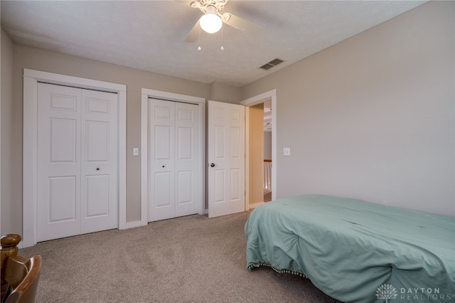 bedroom featuring visible vents, a ceiling fan, a textured ceiling, carpet floors, and multiple closets