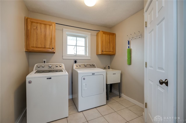 clothes washing area with light tile patterned floors, a textured ceiling, baseboards, cabinet space, and washer and clothes dryer