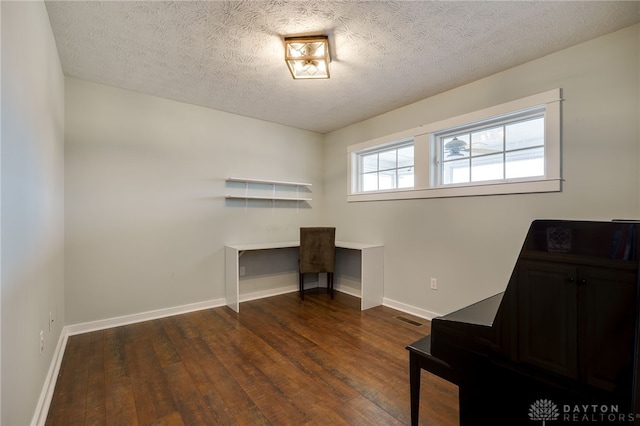 home office with dark wood-style floors, visible vents, a textured ceiling, and baseboards