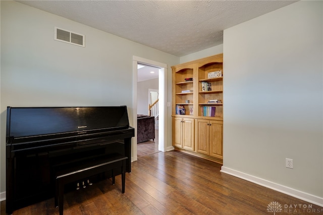 living area featuring dark wood-style floors, a textured ceiling, visible vents, and baseboards