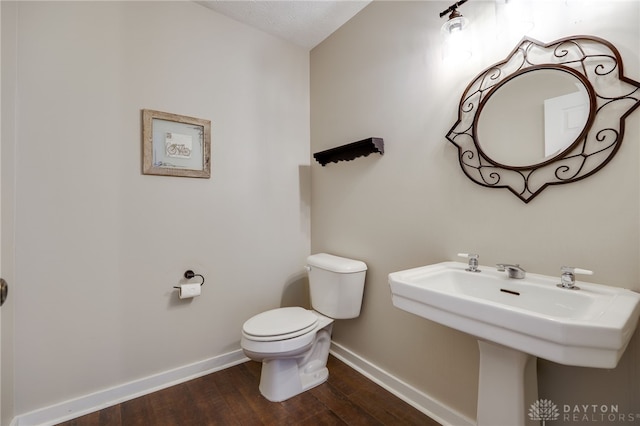 half bathroom with a sink, toilet, baseboards, and wood finished floors