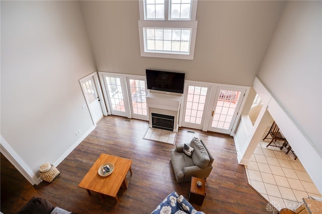 living area with a fireplace with flush hearth, a healthy amount of sunlight, a towering ceiling, and wood finished floors