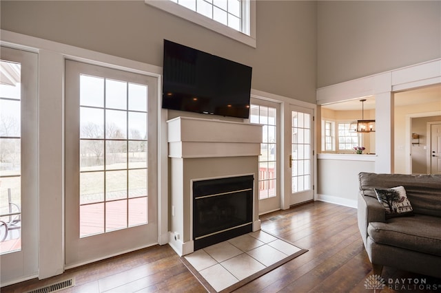 living area with visible vents, hardwood / wood-style floors, a high ceiling, a glass covered fireplace, and baseboards