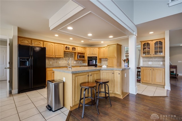 kitchen with light wood finished floors, glass insert cabinets, black appliances, backsplash, and recessed lighting