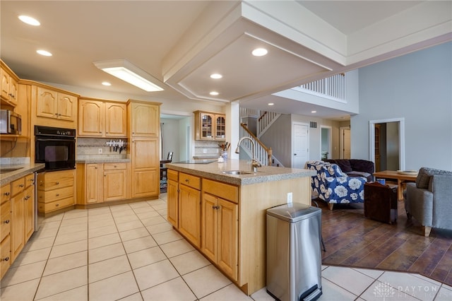 kitchen featuring light tile patterned floors, glass insert cabinets, oven, light brown cabinets, and a sink