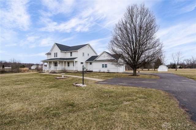 view of front facade featuring a detached garage, a storage unit, a porch, an outdoor structure, and a front lawn