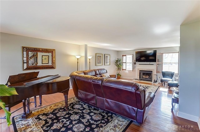 living room featuring a fireplace with flush hearth, baseboards, and wood finished floors