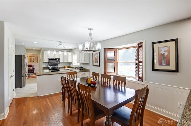 dining room featuring light wood-style floors, recessed lighting, a wainscoted wall, and an inviting chandelier